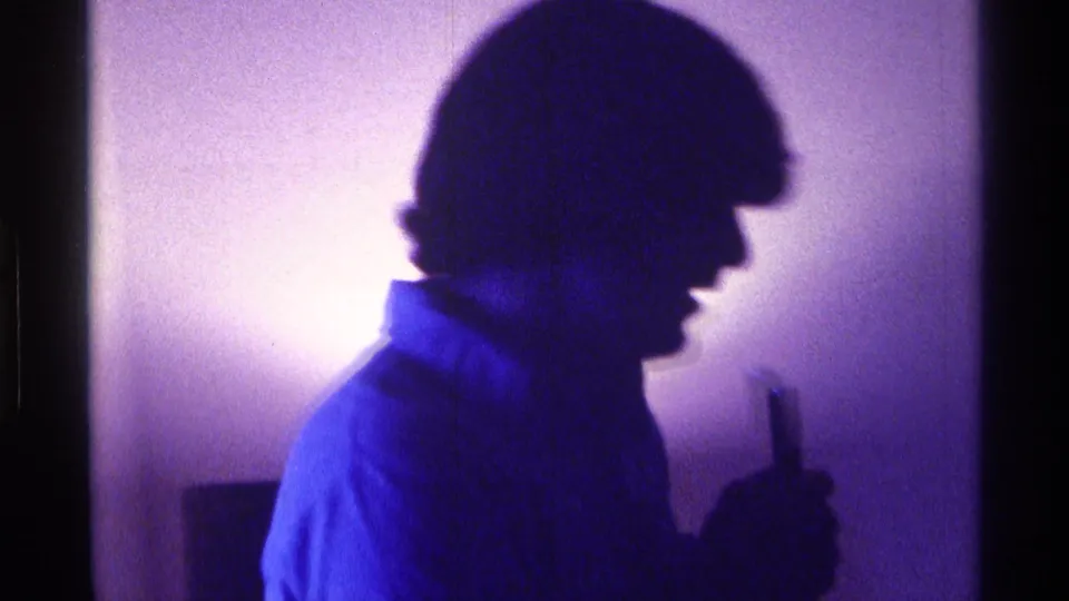 Blurred side view of the young man holding a microphone during a blue-lit 1976 Kentucky house party moment.