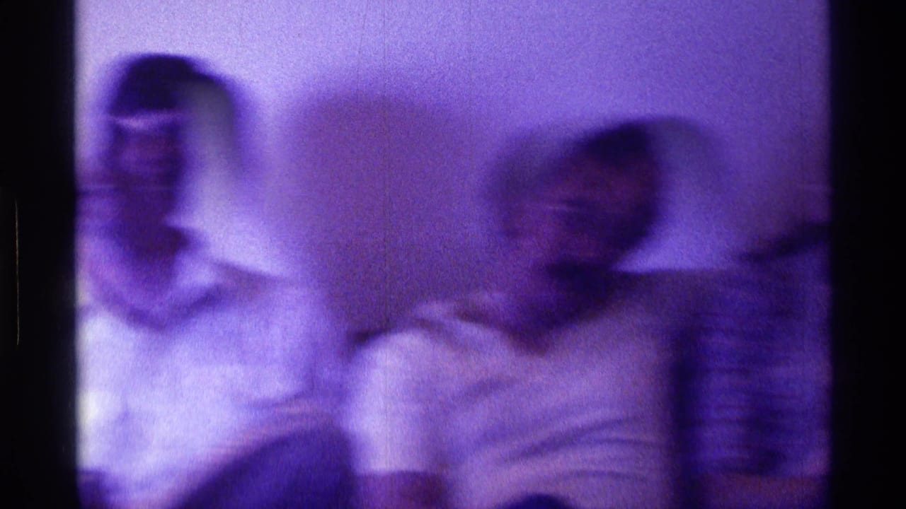 Blurred young adults seated on a couch in a purple-tinted interior.