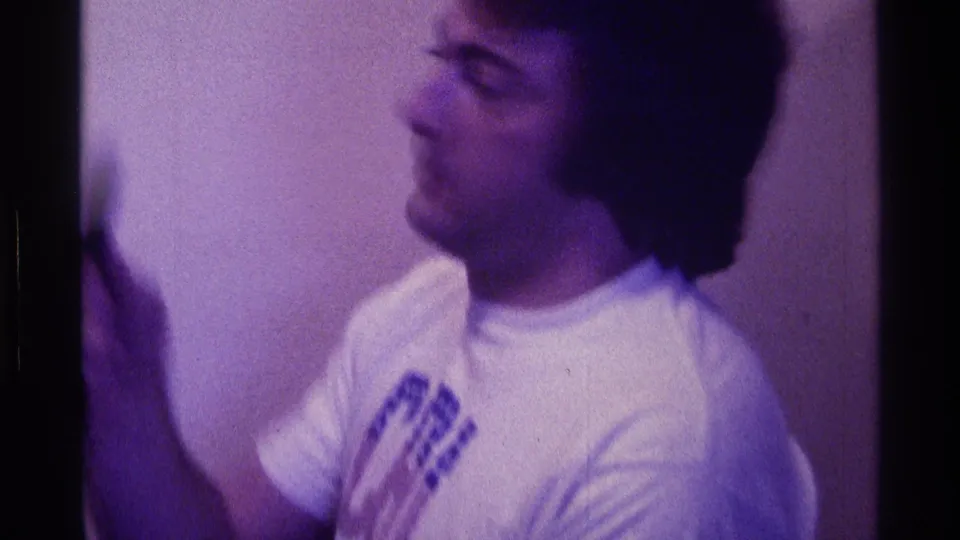 At the end of the clip, the man turns away in profile with the microphone raised, leaving his face partly blurred by motion.