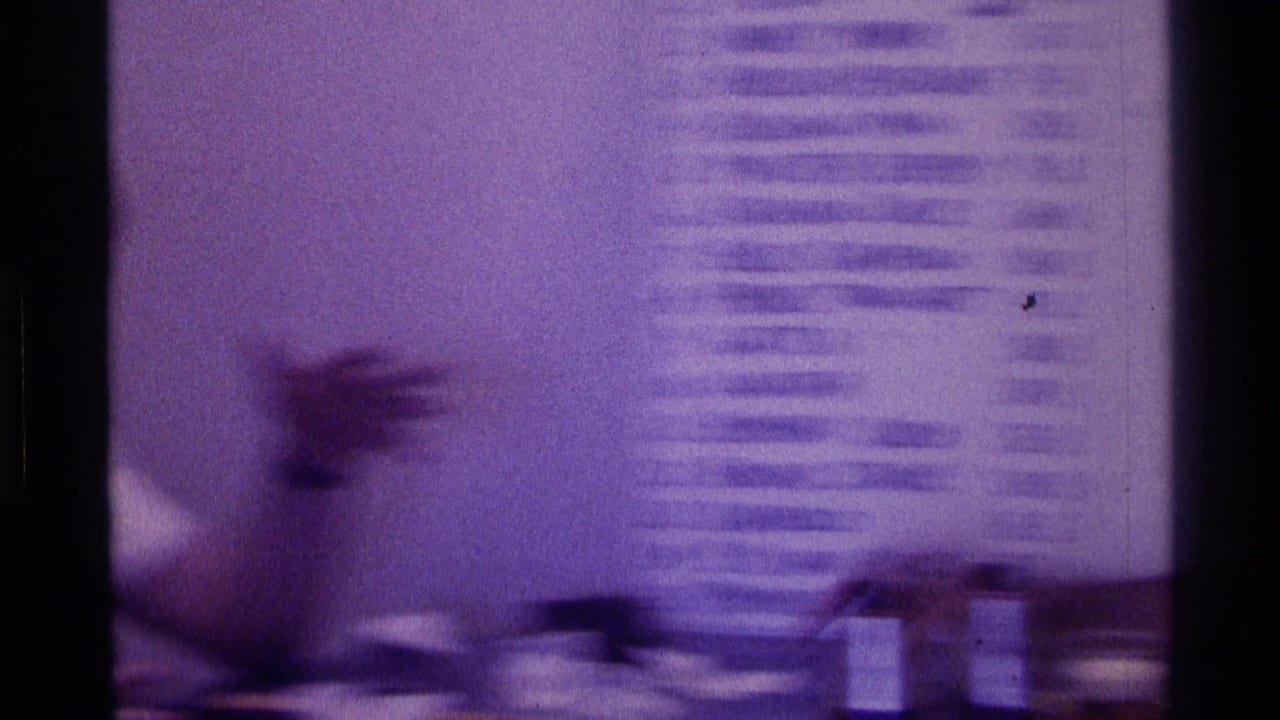Blurred young man at a table beside a wall-mounted handwritten list.