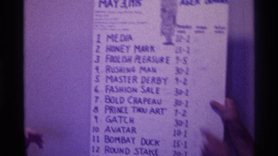 Close 8mm view of a handwritten list with names and numbers, likely connected to a game or scoring activity in the indoor gathering.
