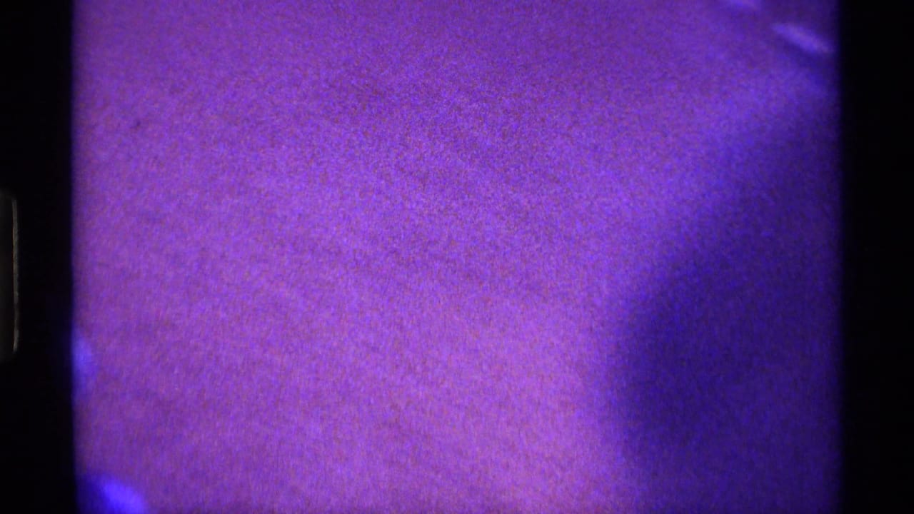Purple-blue close view of a dim interior with film borders and little readable detail.