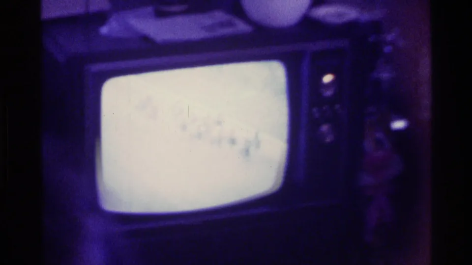 Kentucky 1976 8mm frame of a bright CRT television in a dark living room, with part of a person visible near the right side.