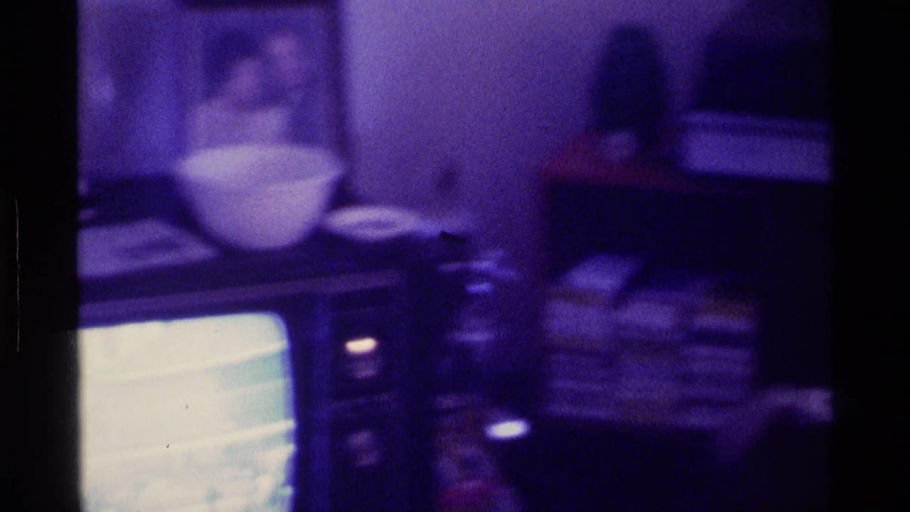 CRT television on a cabinet with a bowl and papers in a dim purple-tinted room.