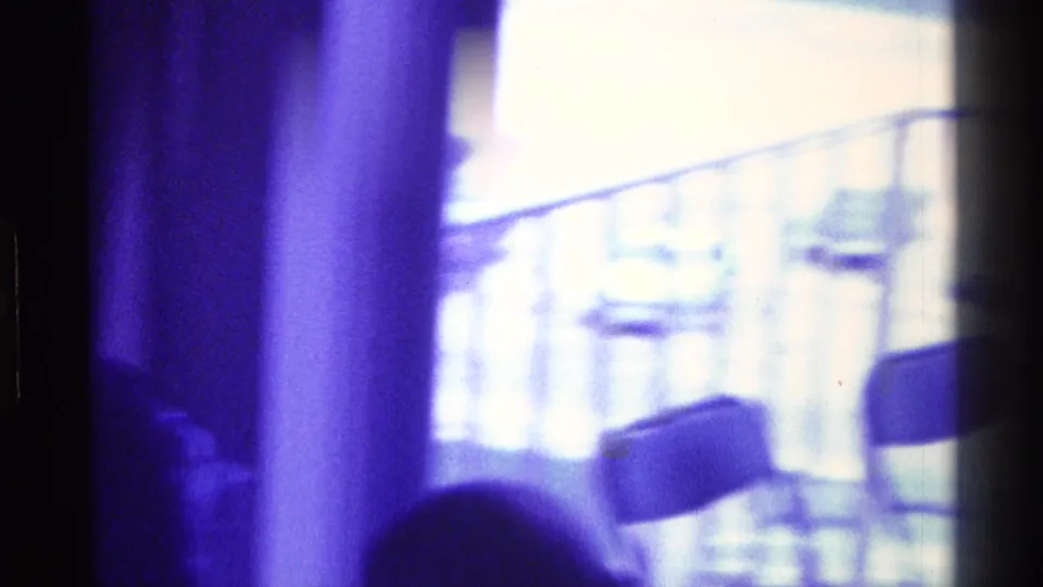 Purple-tinted 1976 Kentucky interior frame with silhouetted figures near bright windows, folding chairs, and an exterior railing.