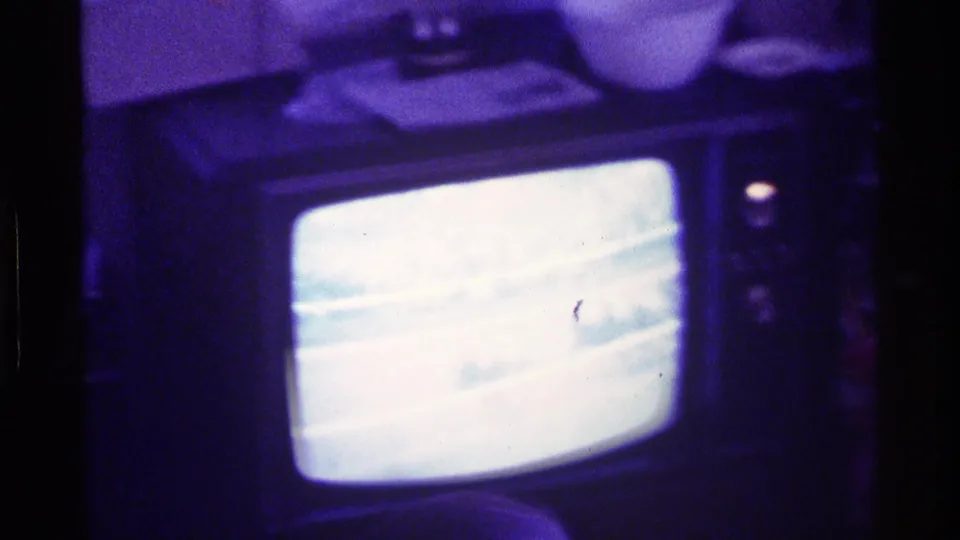 1976 Kentucky home-movie frame of a CRT television glowing in a dark room while a horse race appears on the screen.