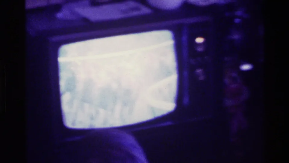 The CRT screen shows a washed-out horse race broadcast, surrounded by dark furniture and indistinct room details.