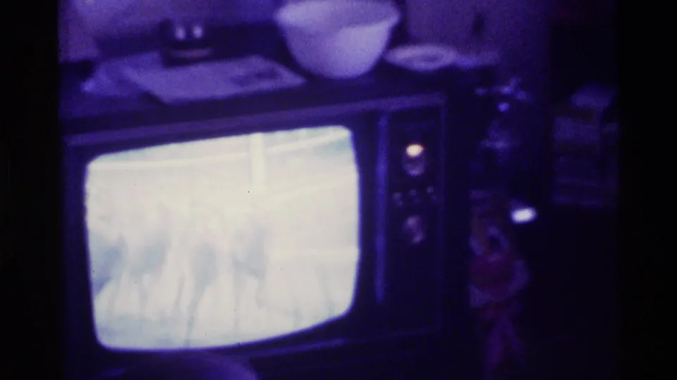 A person is partly visible beside the CRT television as the bright horse race broadcast continues in the dim Kentucky interior.
