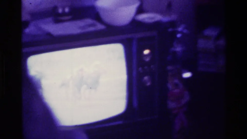 A person sits near the CRT television in a dark 1976 Kentucky home interior while the horse race broadcast blooms on screen.