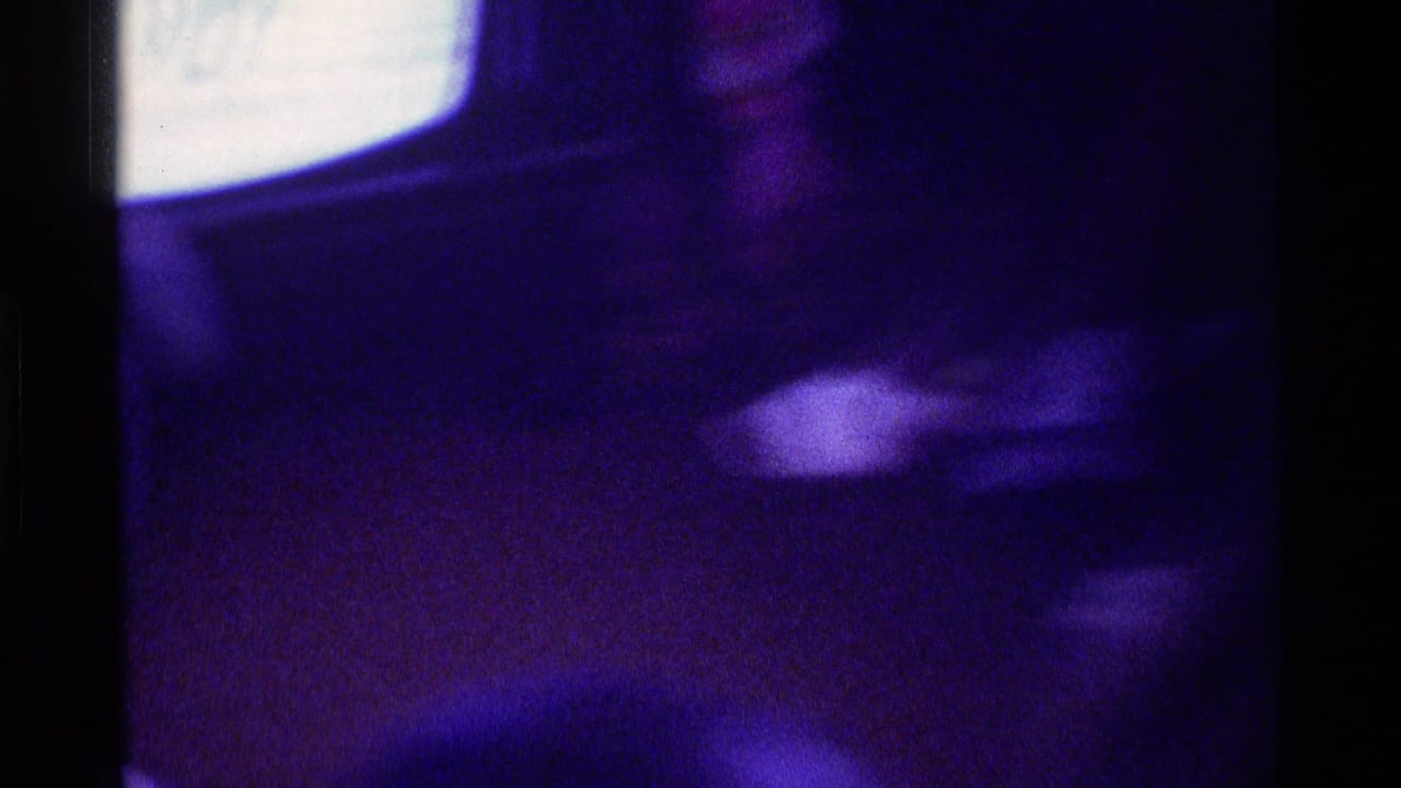 Dark purple-tinted interior with a partial glowing television screen at the upper left.
