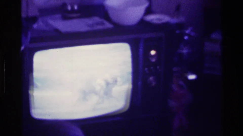 A 1976 Kentucky home-movie frame centers a CRT television showing an indistinct horse-race broadcast in a dim interior.