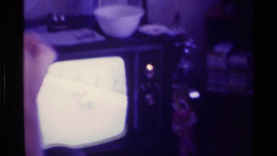 1976 Kentucky interior with a boxy television glowing beneath household items on a cabinet or shelf.