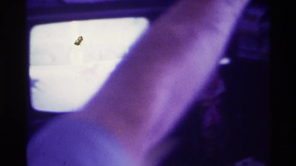 A close forearm crosses the bright television screen in a dark Kentucky living-room home movie from 1976.