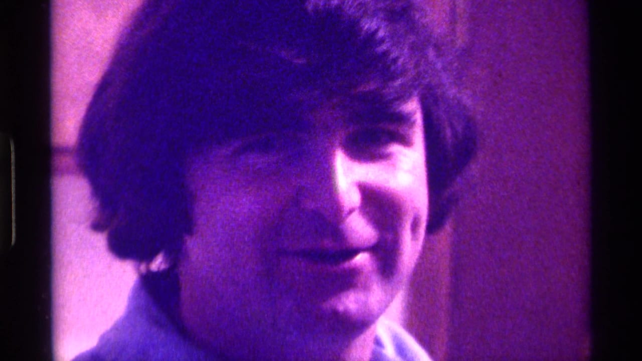 Young man with dark wavy hair looks toward the camera in purple-tinted 8mm footage.