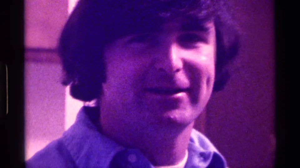 The 1976 Kentucky 8mm frame shows the young man smiling slightly at the camera, with visible grain and magenta-purple color shift.