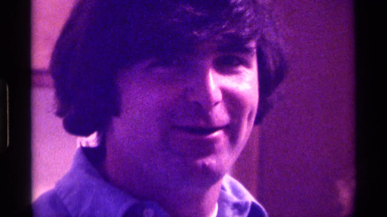 Young man in a blue collared shirt faces the camera under purple indoor light.