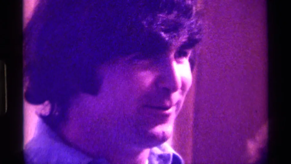 The young man appears in three-quarter view, softly lit in purple-blue tones in this Kentucky 1976 home-movie frame.