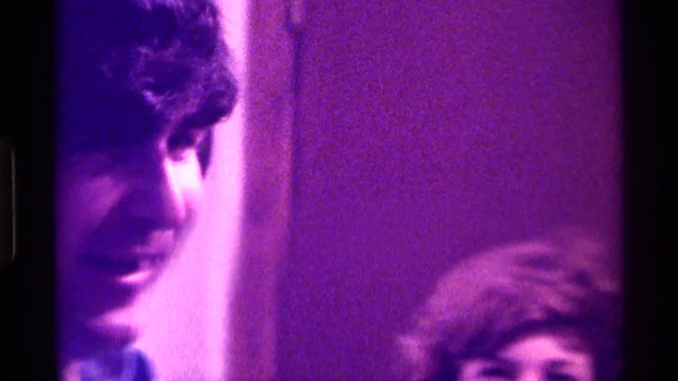 A cropped 1976 Kentucky home-movie frame shows the young man's face at left and another partially visible person low in the shot.