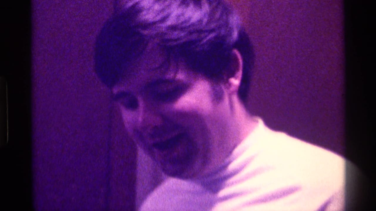 Young man in a white turtleneck smiles while standing indoors in 1976 Kentucky home-movie footage.