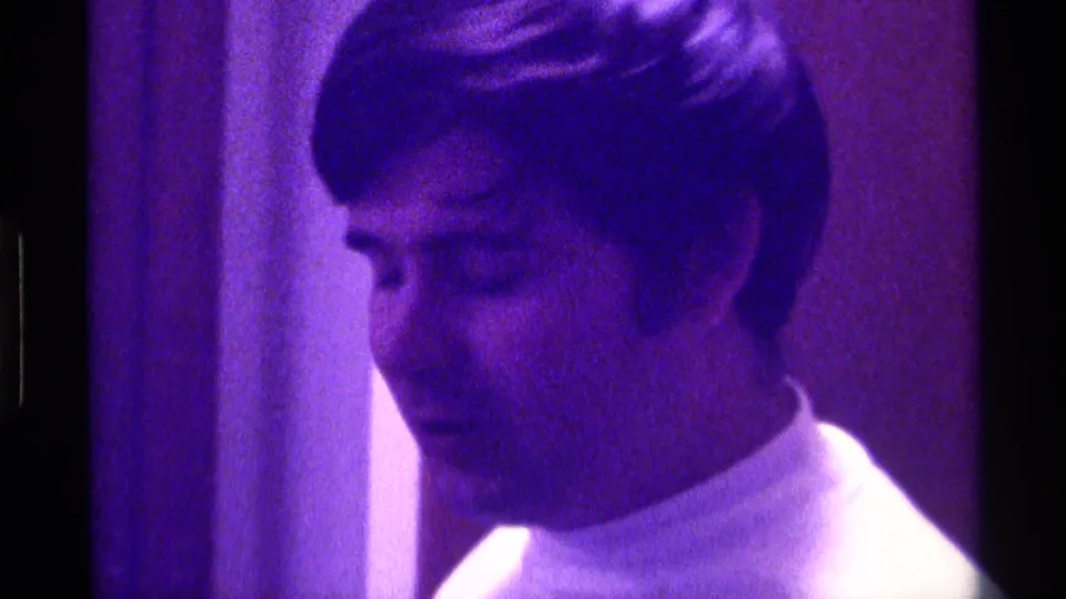 The performer turns slightly downward in a purple-lit Kentucky 8mm frame from 1976.