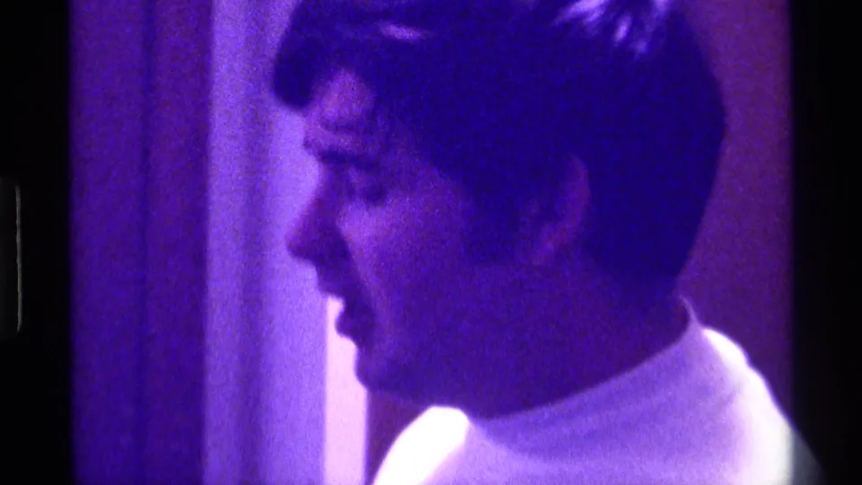 Purple-lit profile of a man who appears to be singing or speaking in 1976 Kentucky 8mm footage.