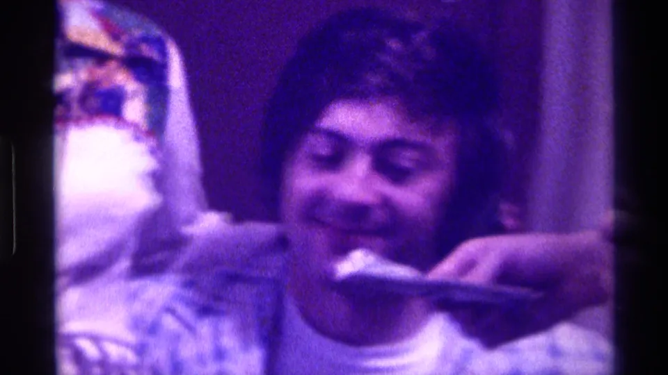 Smiling young man in a patterned shirt while a hand holds a dollar bill near his face in 1976 Kentucky footage.