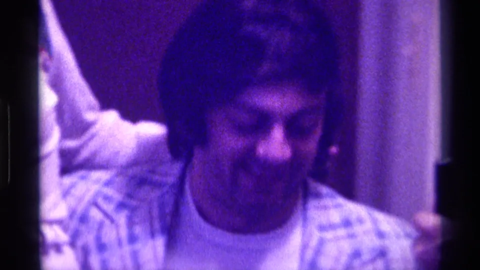 1976 Kentucky 8mm frame of a man looking down indoors while a nearby hand appears to hold folded money.