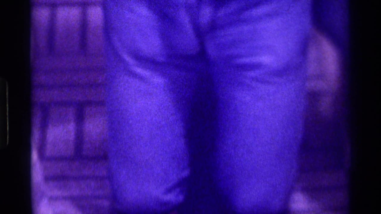 Close view of a person wearing jeans or trousers in a dim purple-tinted room.