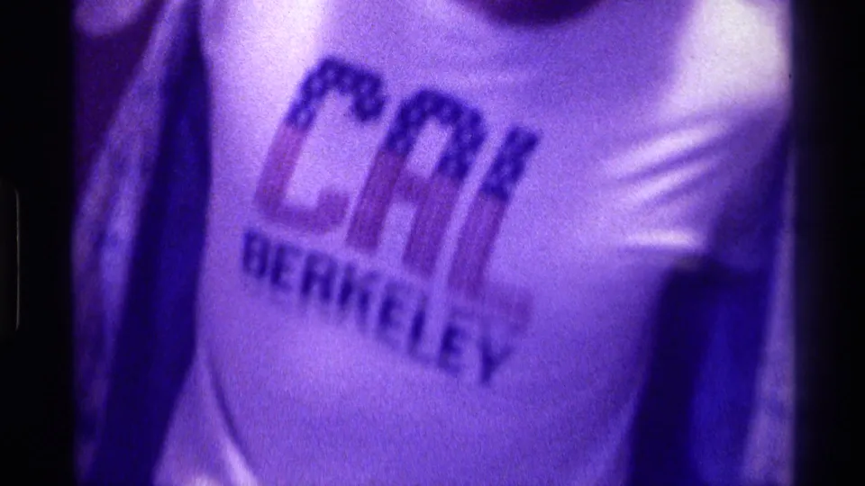 Close 1976 Kentucky home-movie frame of a white CAL BERKELEY T-shirt in purple-tinted low light.