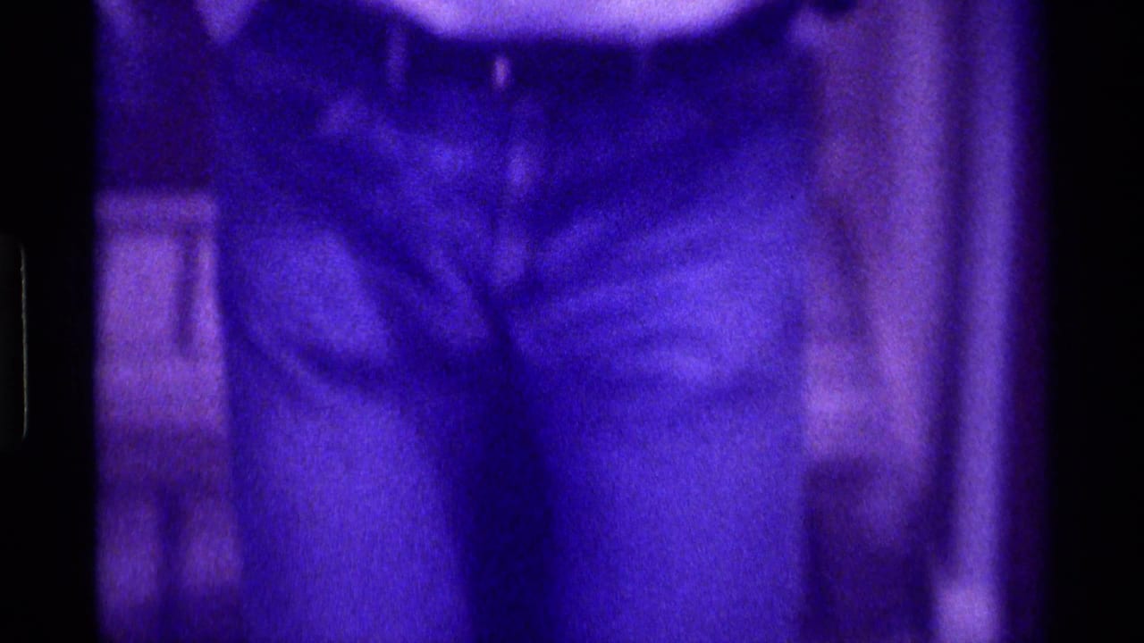 Kentucky 1976 8mm frame showing a person's dark pants and brown shoes on a tiled floor with soft purple color shift.