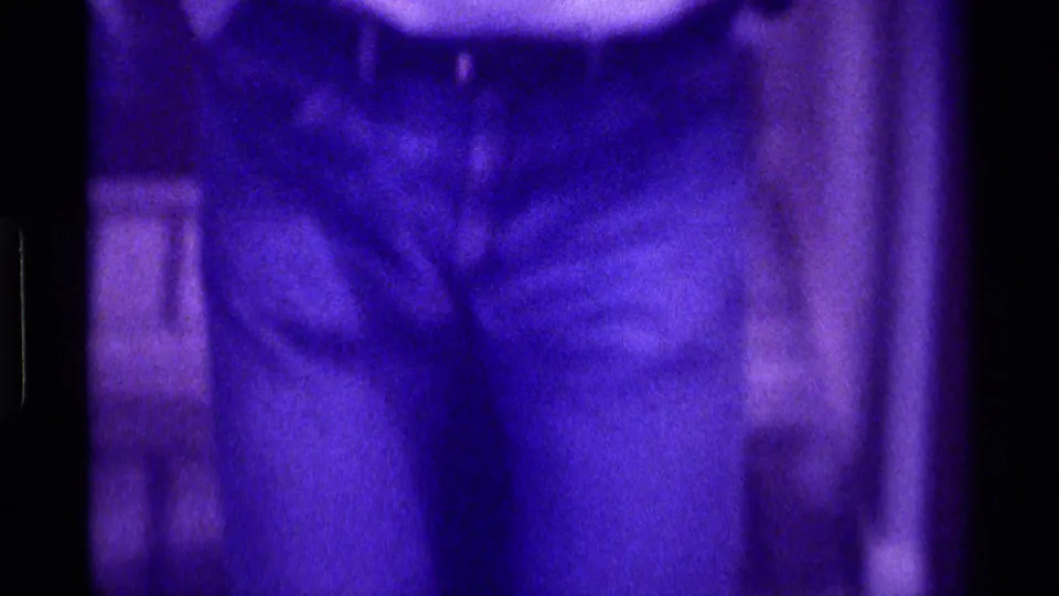 Kentucky 1976 8mm frame showing a person's dark pants and brown shoes on a tiled floor with soft purple color shift.