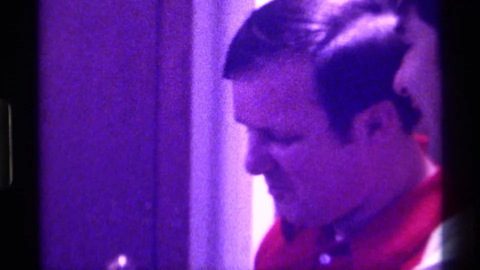 In the final frame, the man in a red polo shirt looks downward beside a doorway in purple-shifted 1976 Kentucky home-movie footage.