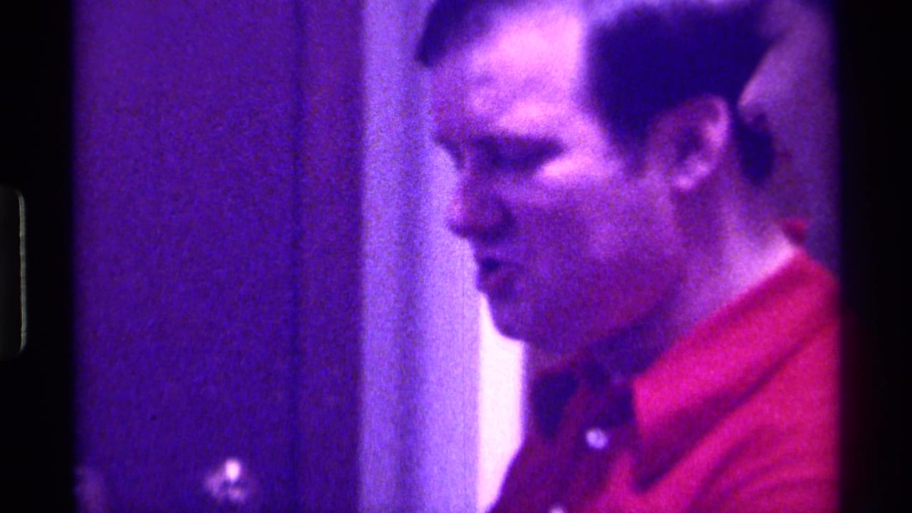 Man in a red shirt seen in profile inside a dim room.