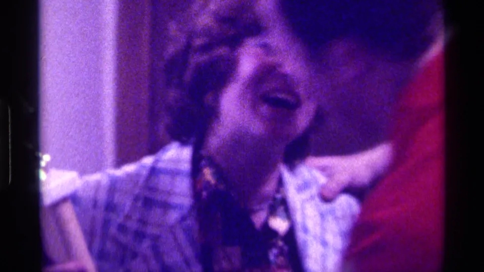 The woman appears to celebrate with an arm raised while another adult in a red shirt partly blocks the foreground.