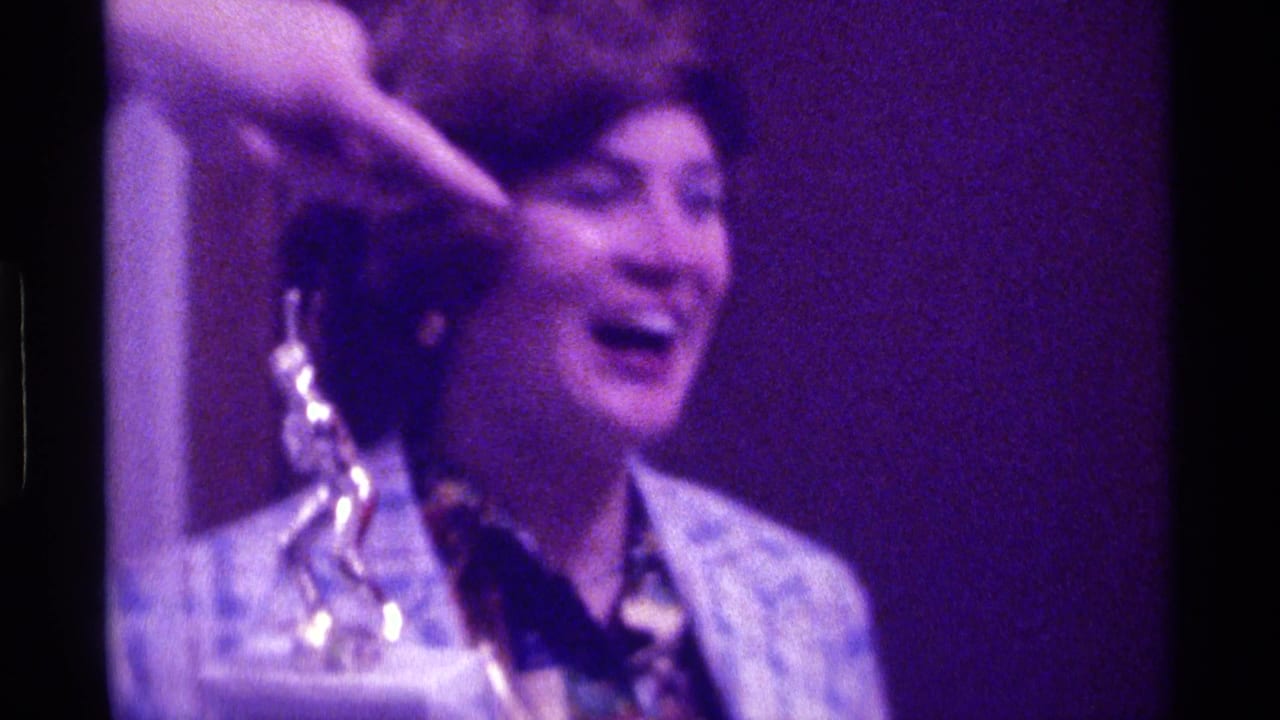 1976 Kentucky home-movie frame showing a smiling woman near a trophy while a hand points across the foreground.