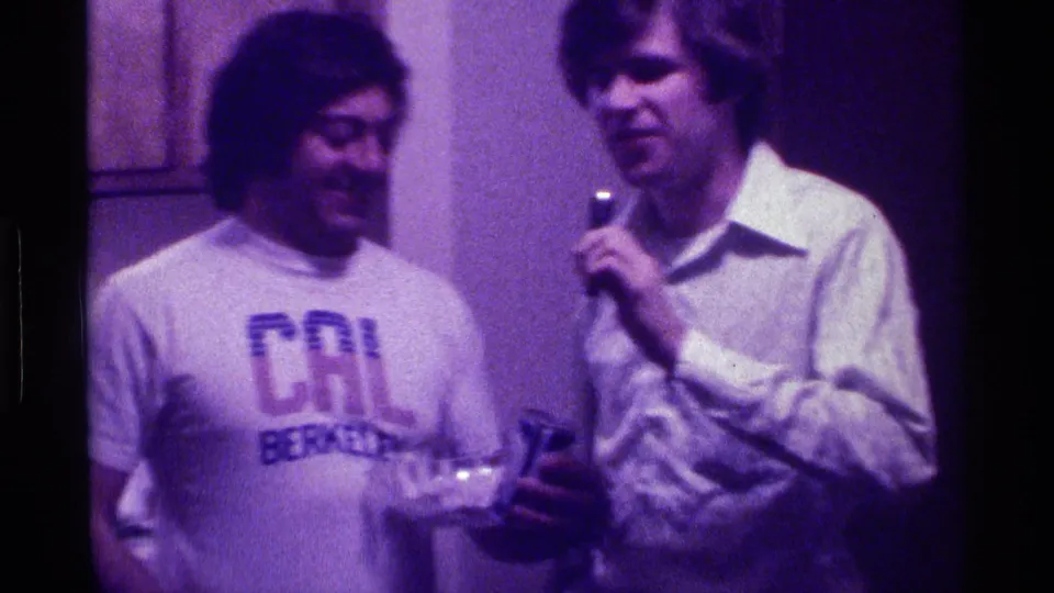 At the end of the 1976 Kentucky clip, the microphone holder stands beside the smiling man in the Cal Berkeley shirt near party glasses.