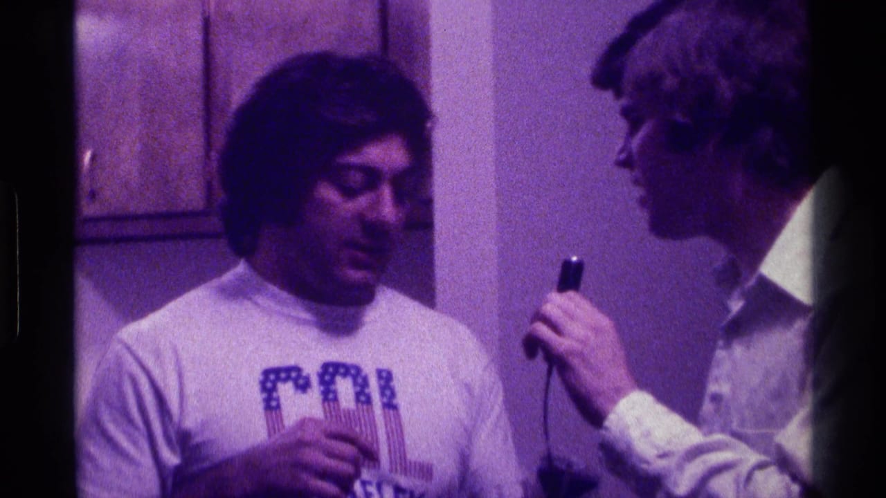 Two young men indoors, one in a CAL Berkeley shirt and one holding a small microphone.