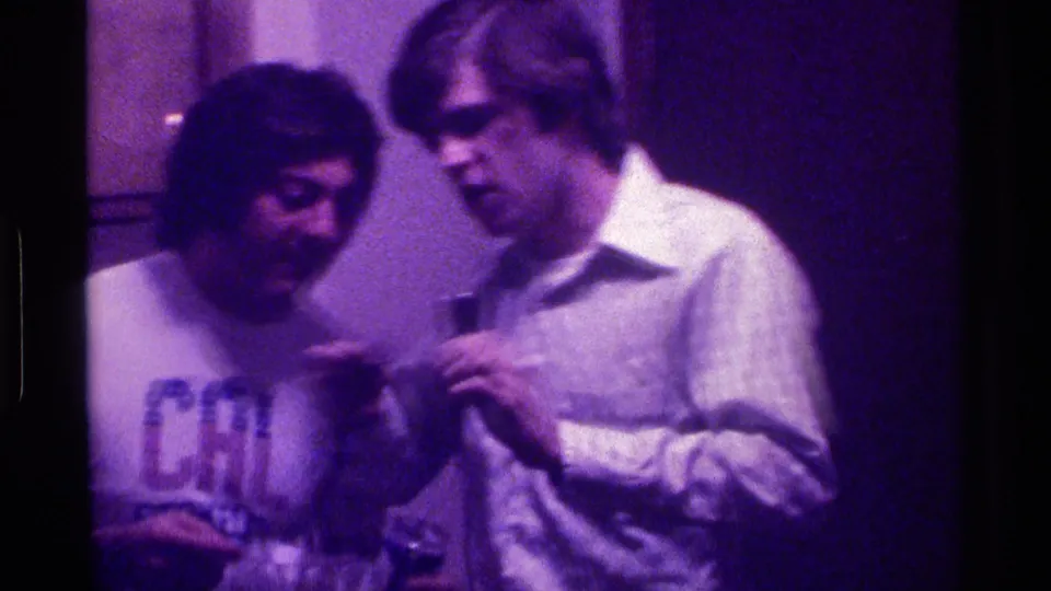 In the final frame, the men stand close in the private room as the light-shirted man holds the small microphone between them.