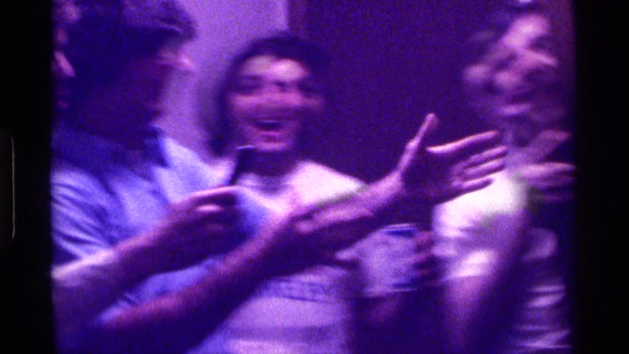 Young men laughing and gesturing in a purple-lit interior.