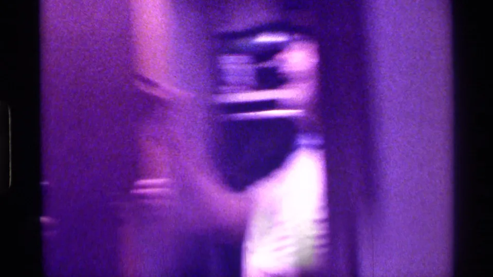 A motion-blurred figure moves through a dim private interior in purple-tinted 8mm home-movie footage.