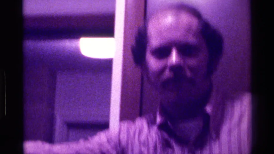 A bearded adult man appears close to the handheld camera inside a dim Kentucky interior with a hanging light behind him.