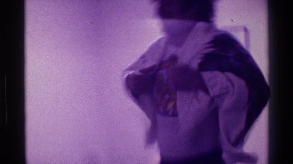 In the 1976 Kentucky home-movie scene, a man moves playfully while holding or wearing a draped sheet or jacket like a cape.