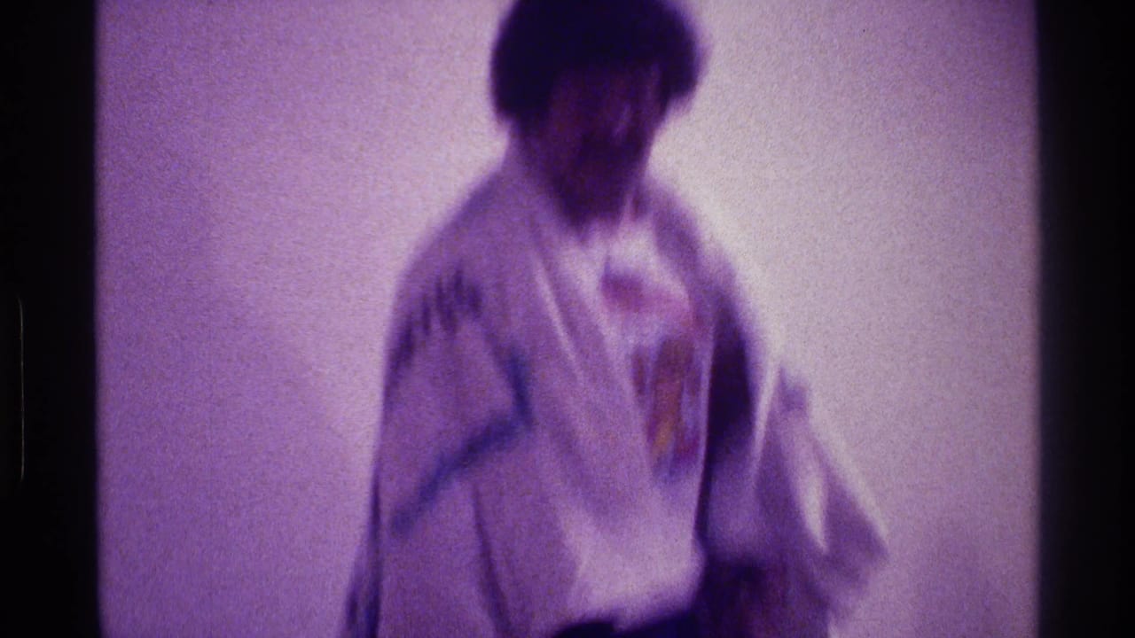 Soft 8mm frame of a man in patterned fabric moving indoors in the Kentucky home-movie scene.