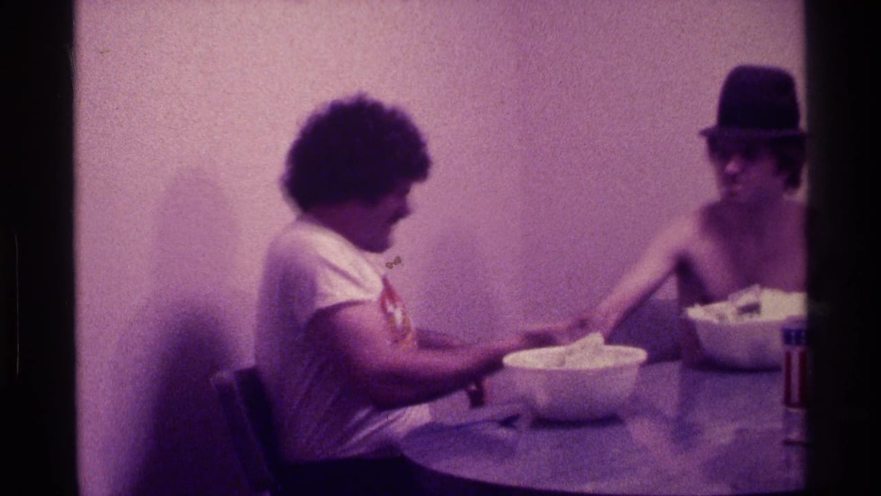Two young men sit at a round table with white bowls in a dim interior.
