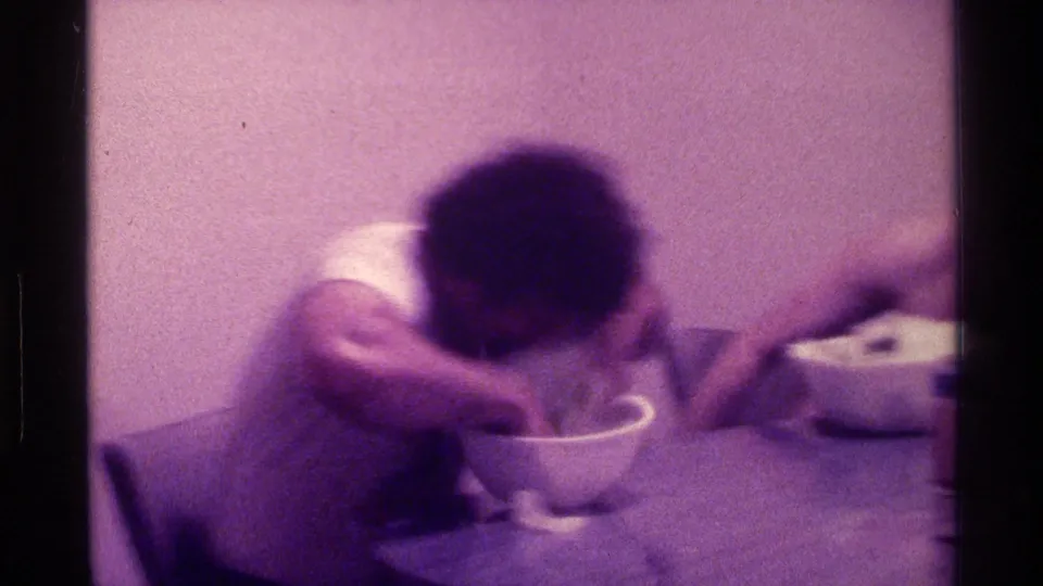 1976 Kentucky home-movie frame of a participant leaning into a bowl on a table during an informal food-table competition.