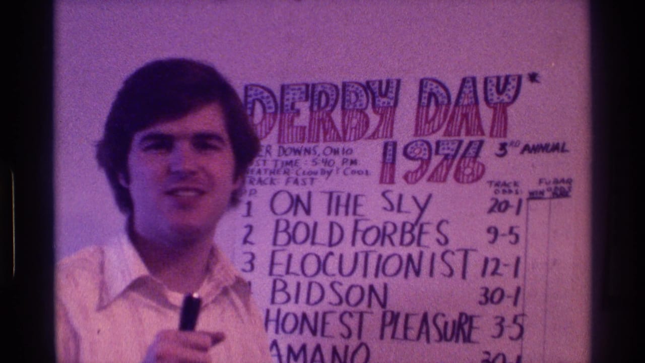 In 1976 Kentucky home-movie footage, a man in a white collared shirt faces the camera while holding a microphone beside a handwritten Derby Day poster.
