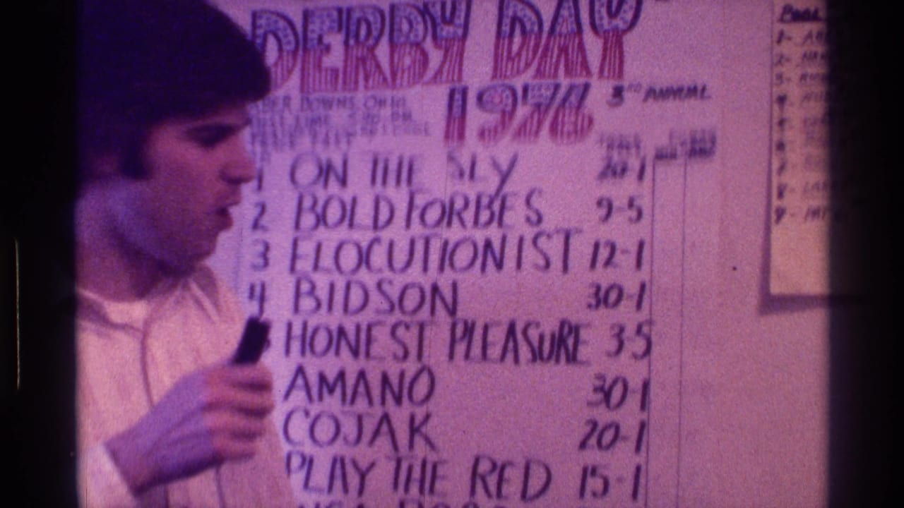 Man holds a microphone and looks toward a handwritten race lineup poster.