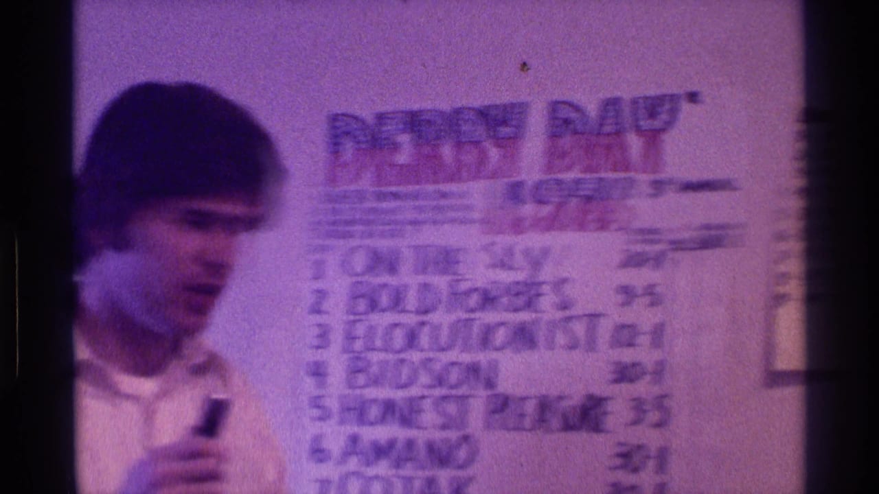 Blurred man with microphone stands near the Derby Day board and handwritten odds.