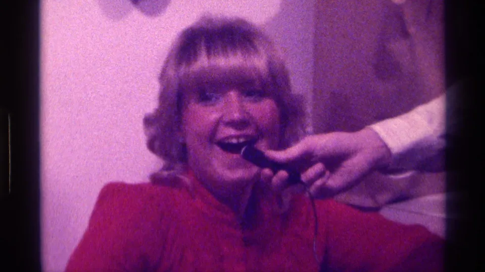 The woman laughs during the informal Kentucky home interview, with the microphone close to her mouth and the interior softly lit.