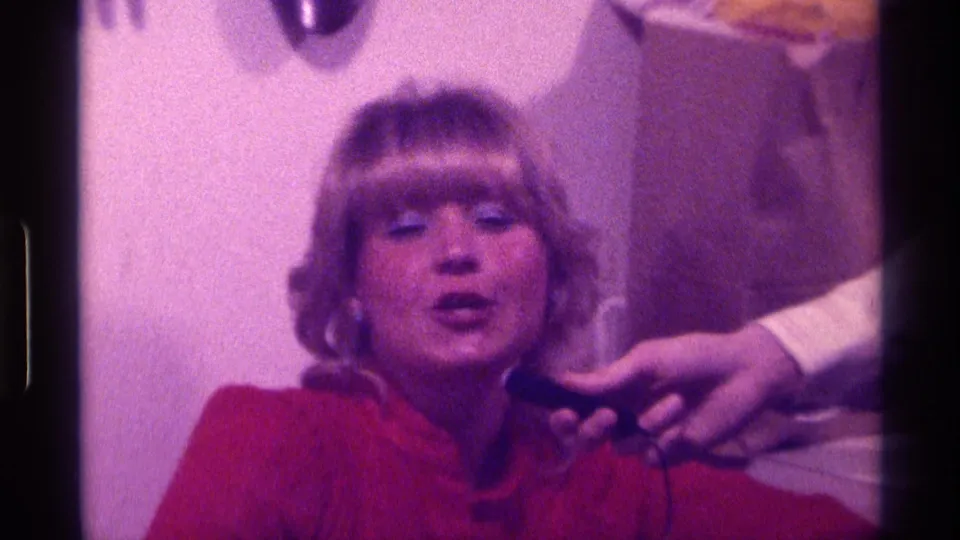 A close 8mm frame shows the woman facing the camera during the informal 1976 Kentucky singing moment.
